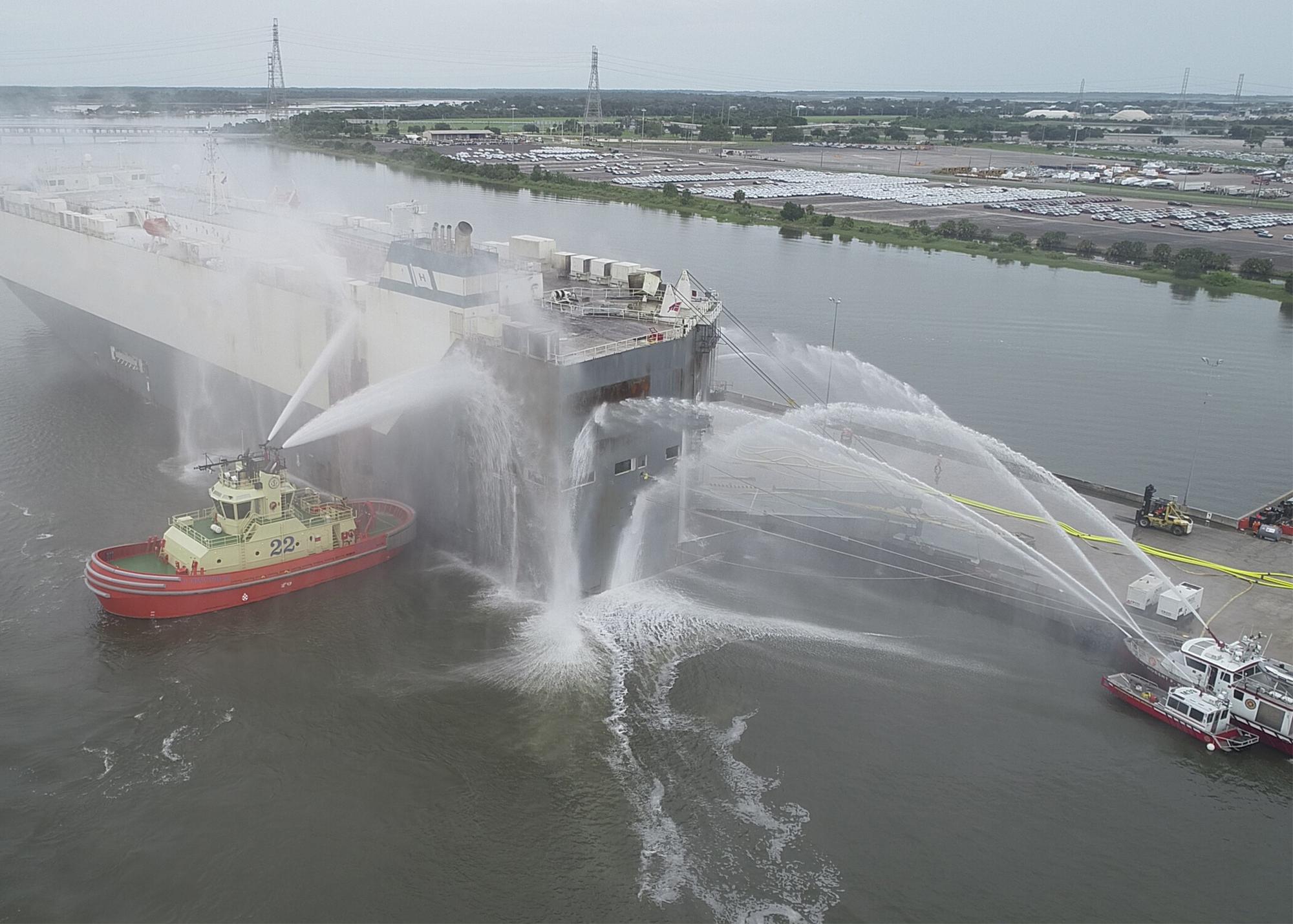 Tugboat spraying water on a docked car carrier during port firefighting operations
